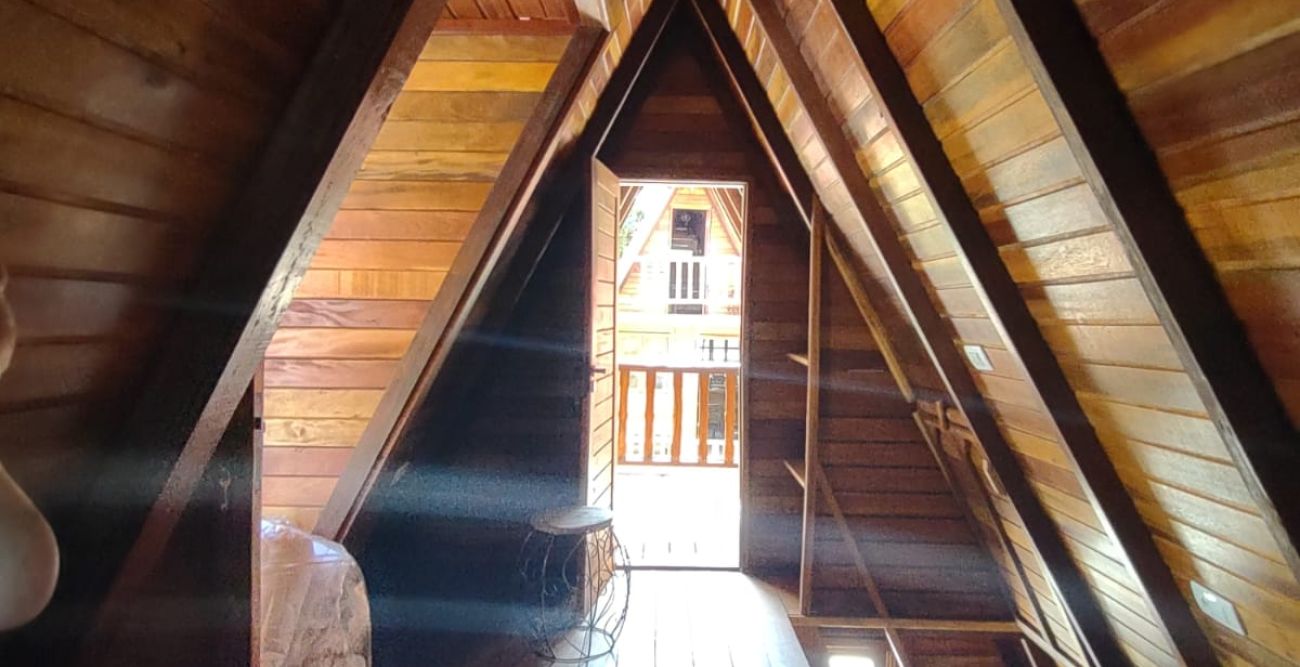 Quarto do chalé, com cama de casal sob o telhado de madeira