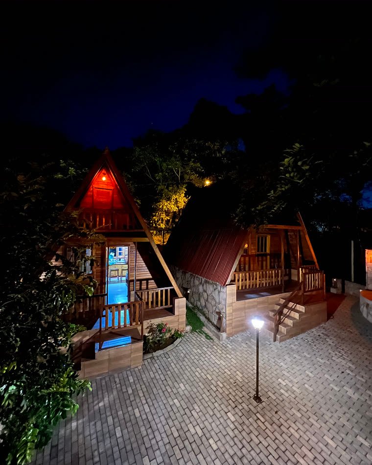 Chalés iluminados ao anoitecer, com piso de pedra e jardim
