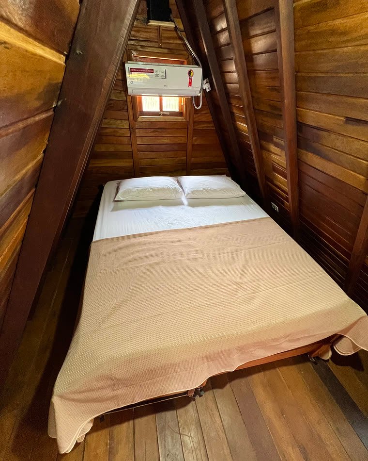 Quarto do chalé com cama arrumada, janela pequena e ar-condicionado