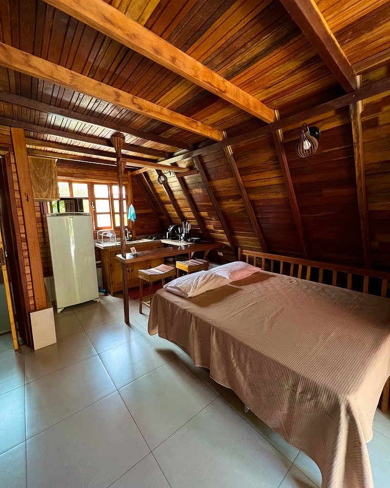 Cama e cozinha integrada no chalé, sob o telhado de madeira